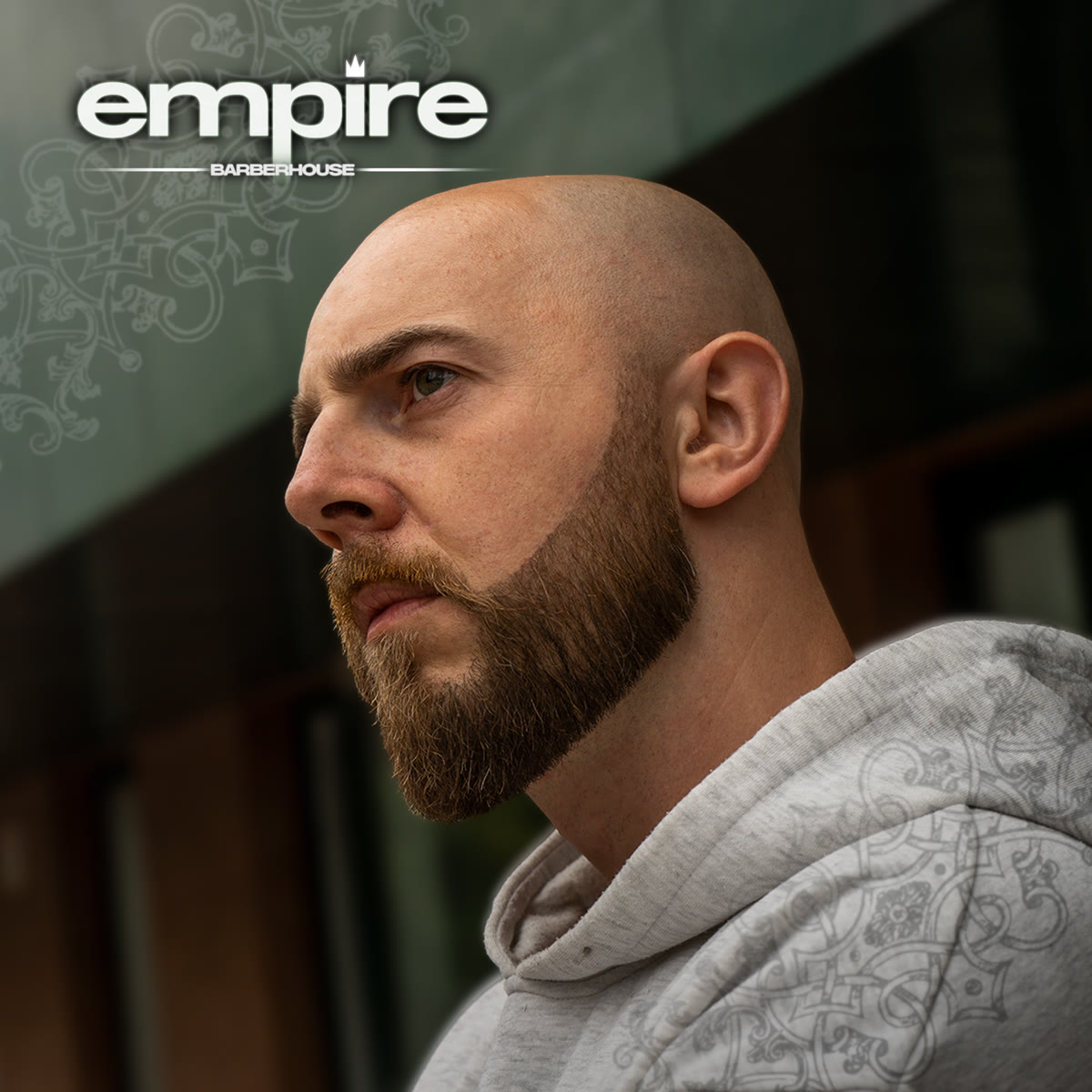 Portret barbera Empire — pełna broda, szary hoodie, spojrzenie w bok.