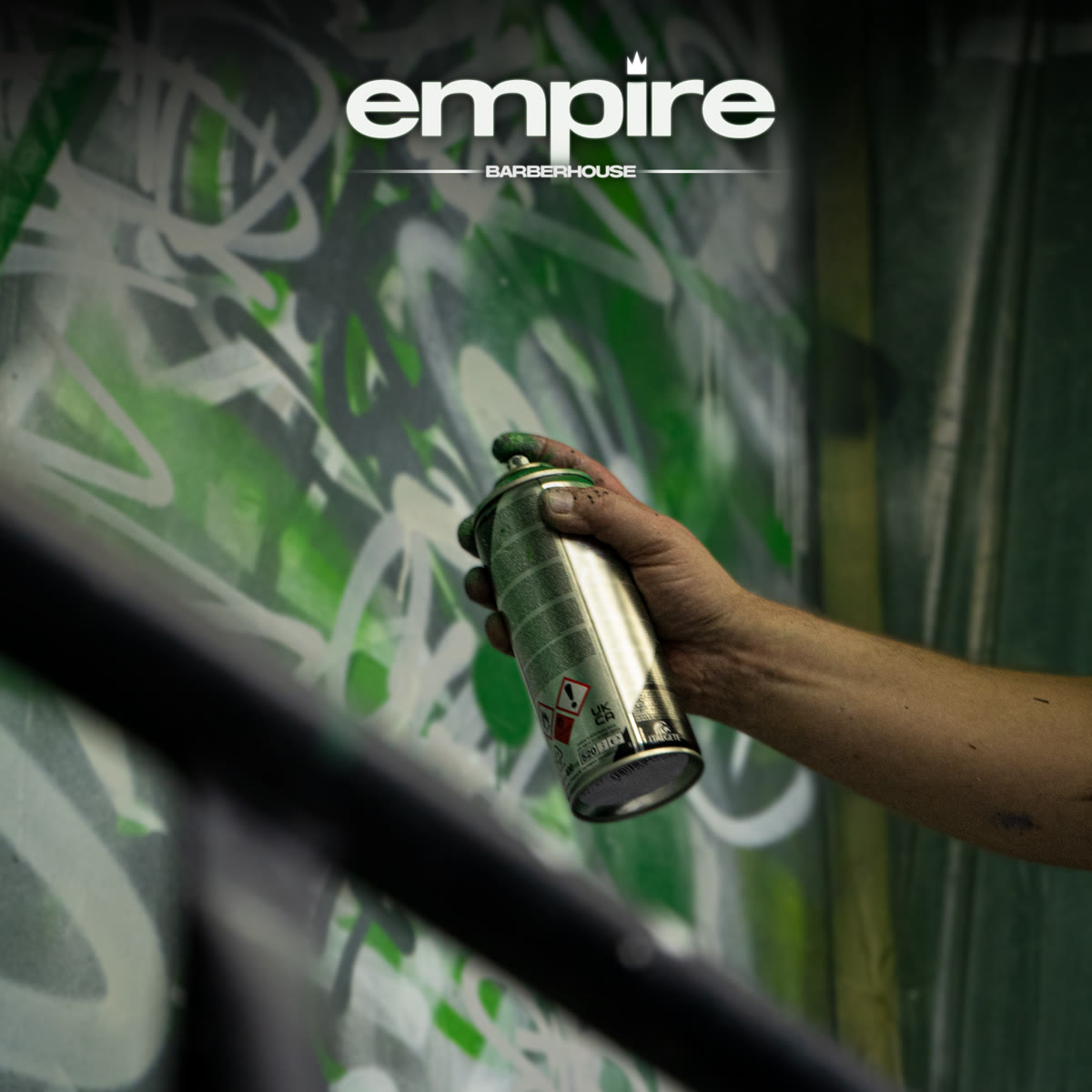 Dłoń ze sprayem przy ścianie pokrytej zielonym graffiti — klimat salonu.