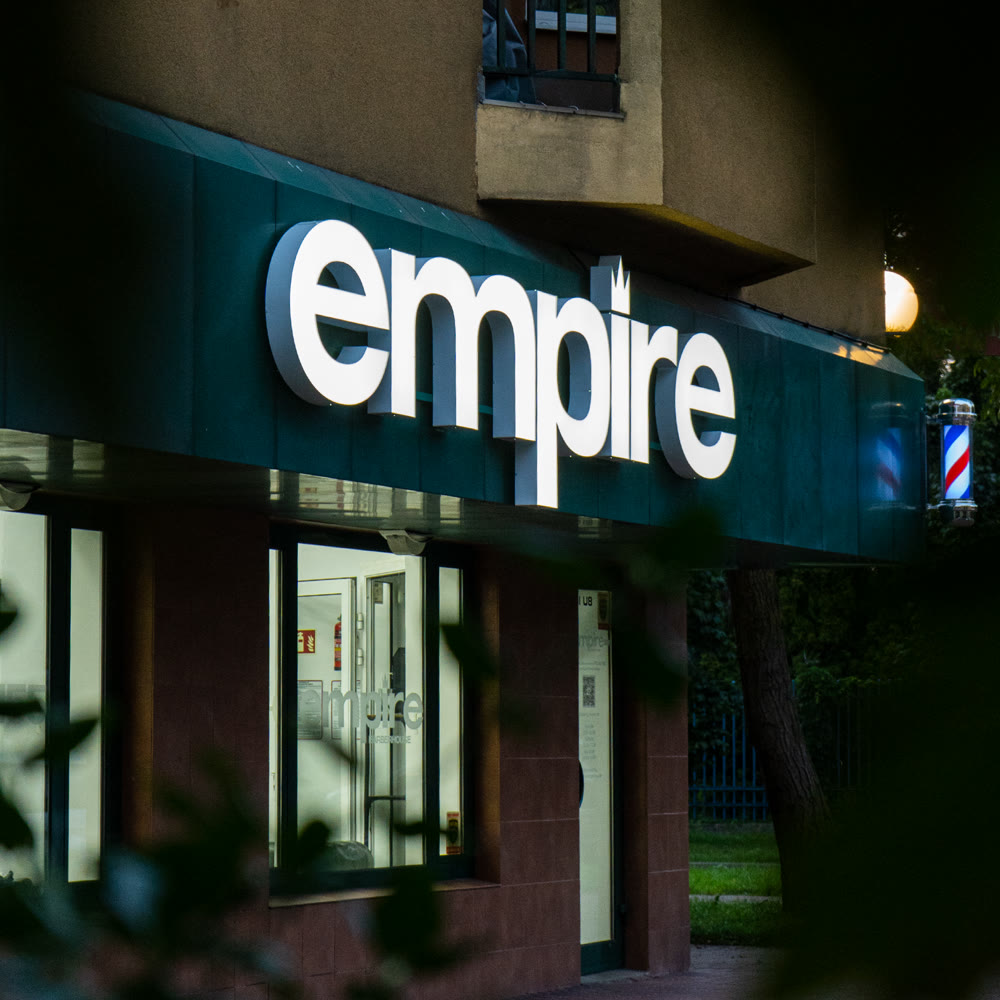 Front salonu Empire Barberhouse po zmroku — podświetlony napis empire nad witryną i kręcący się słupek barberski.