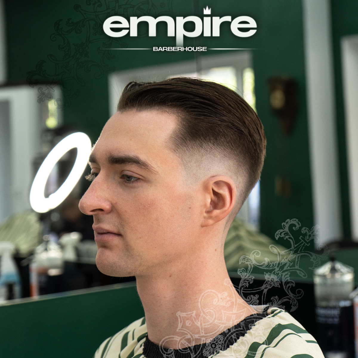 Middle part z niskim fade'em — profil klienta przy podświetlonym lustrze.